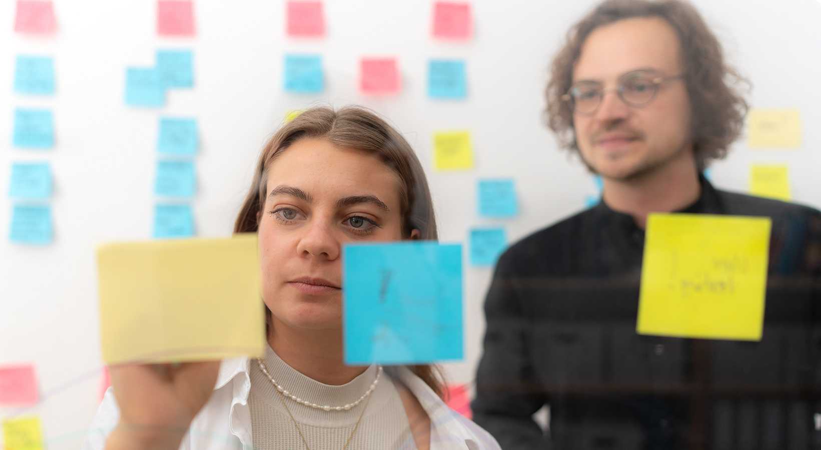 Two person, who are writing on a sticky note.
