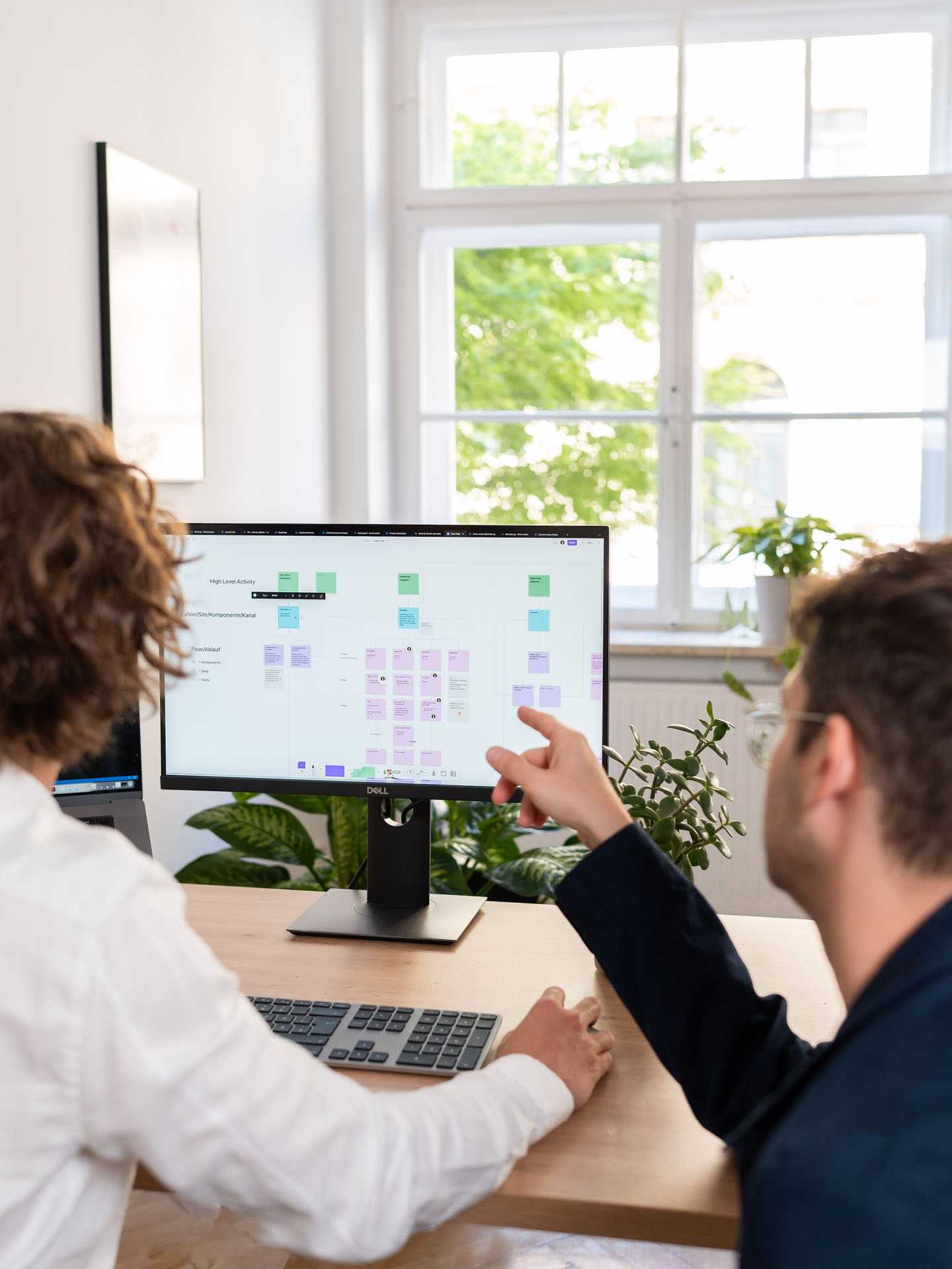 Ein Designer und ein Entwickler sitzen vor einem Laptop. Einer der beiden zeigt auf den Bildschirm.