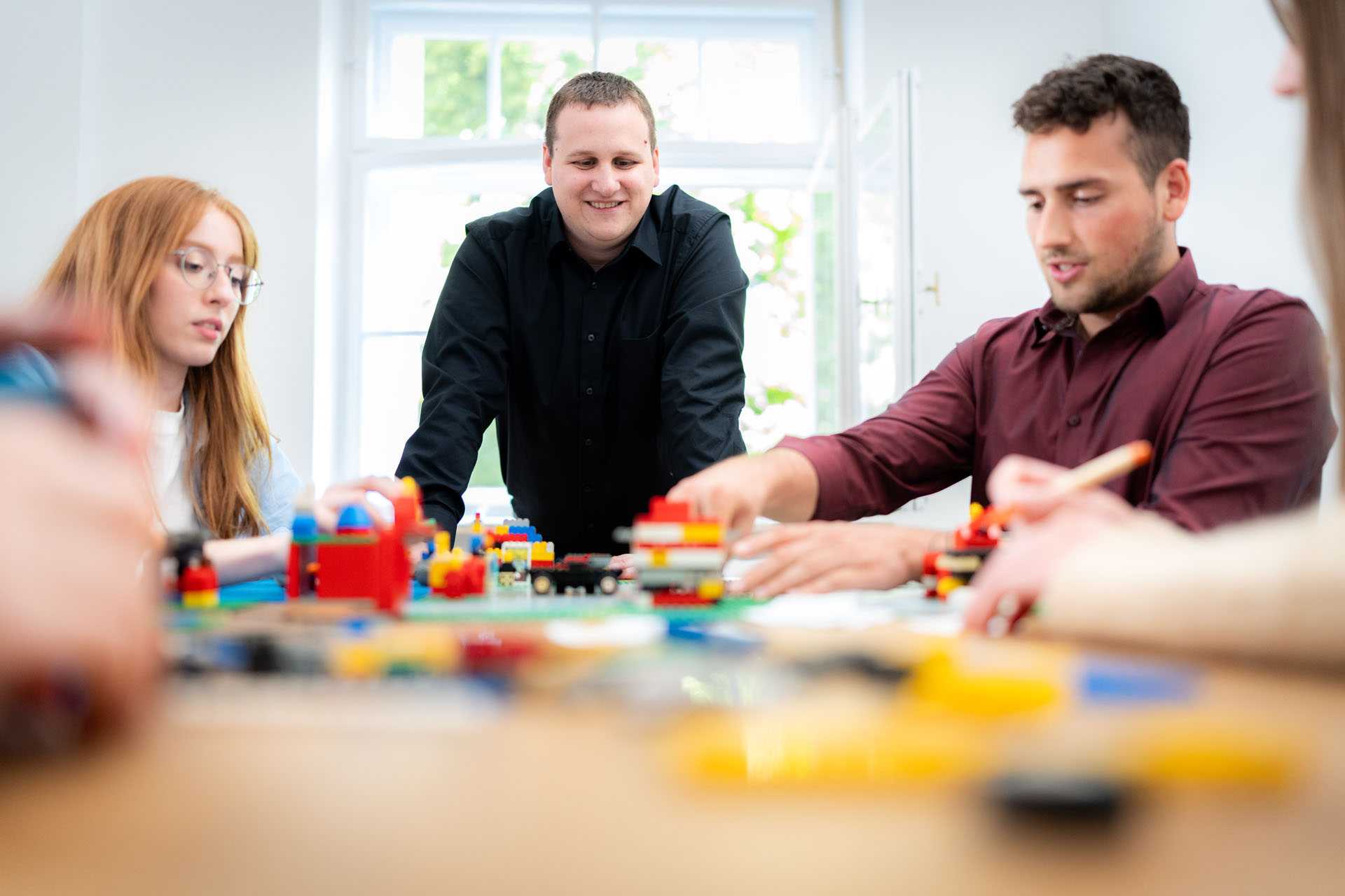 Two people are sitting at a table, while a third person is standing at the end of the table.