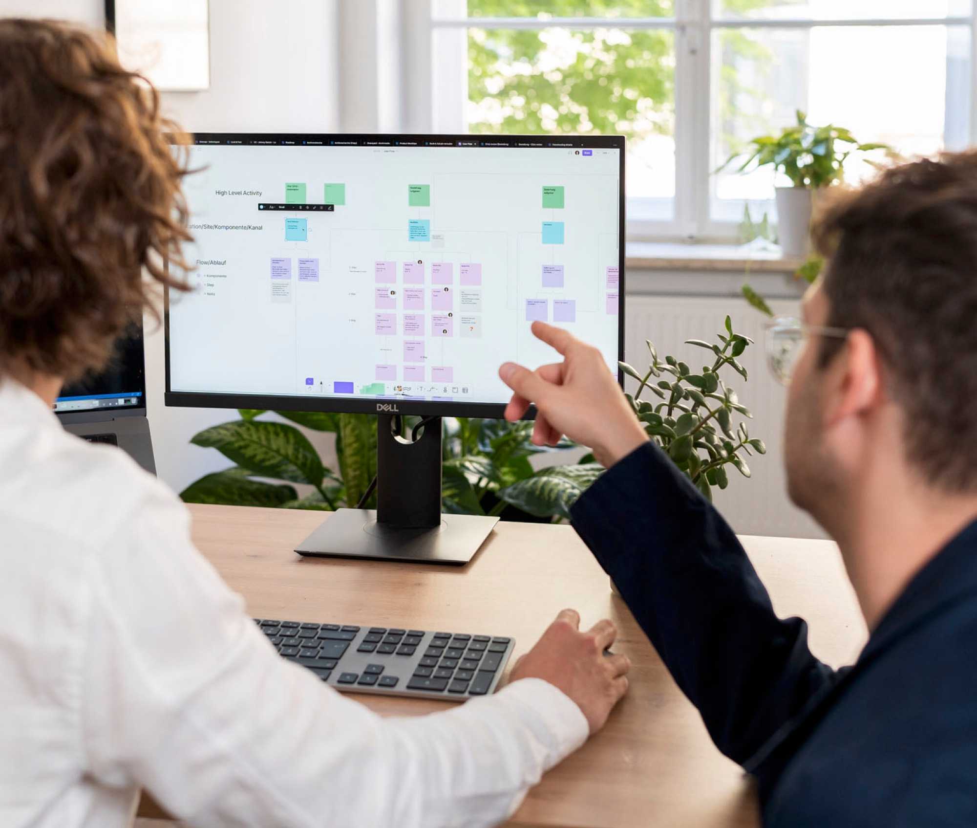 Mitarbeiter Kalle zeigt UX Designer Johnny etwas auf dem Bildschirm.